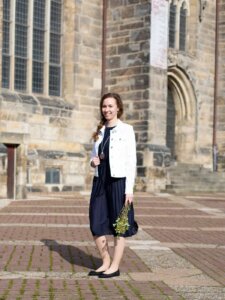 Junge Frau in dunkelblauem Kleid steht vor einer Kirche