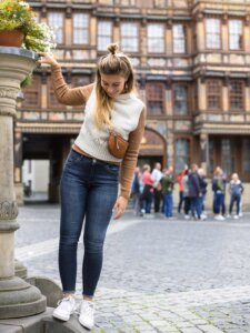 Junge Frau mit hellem Pullunder hält sich stehend an einem Brunnen fest