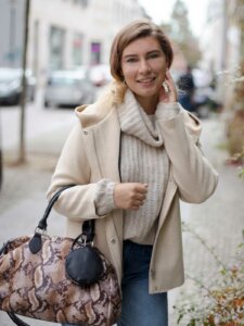 Junge Frau in cremefarbenem Strickpullover, beiger Jacke und große Henkeltasche mit Animalprint