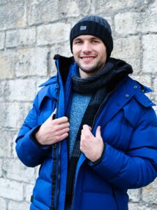 Junger Mann in blauer Winterjacke mit Mütze und Schal