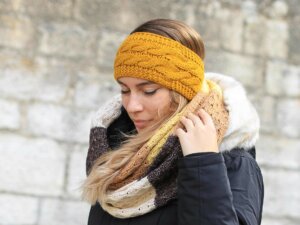 Junge Frau mit senfgelbem Stirnband hebt ihre Hand zu ihrem Schal
