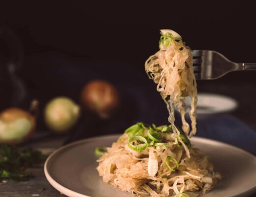 Teller mit Sauerkraut und Lauch, Gabel mit Essen darauf wird darüber gehalten