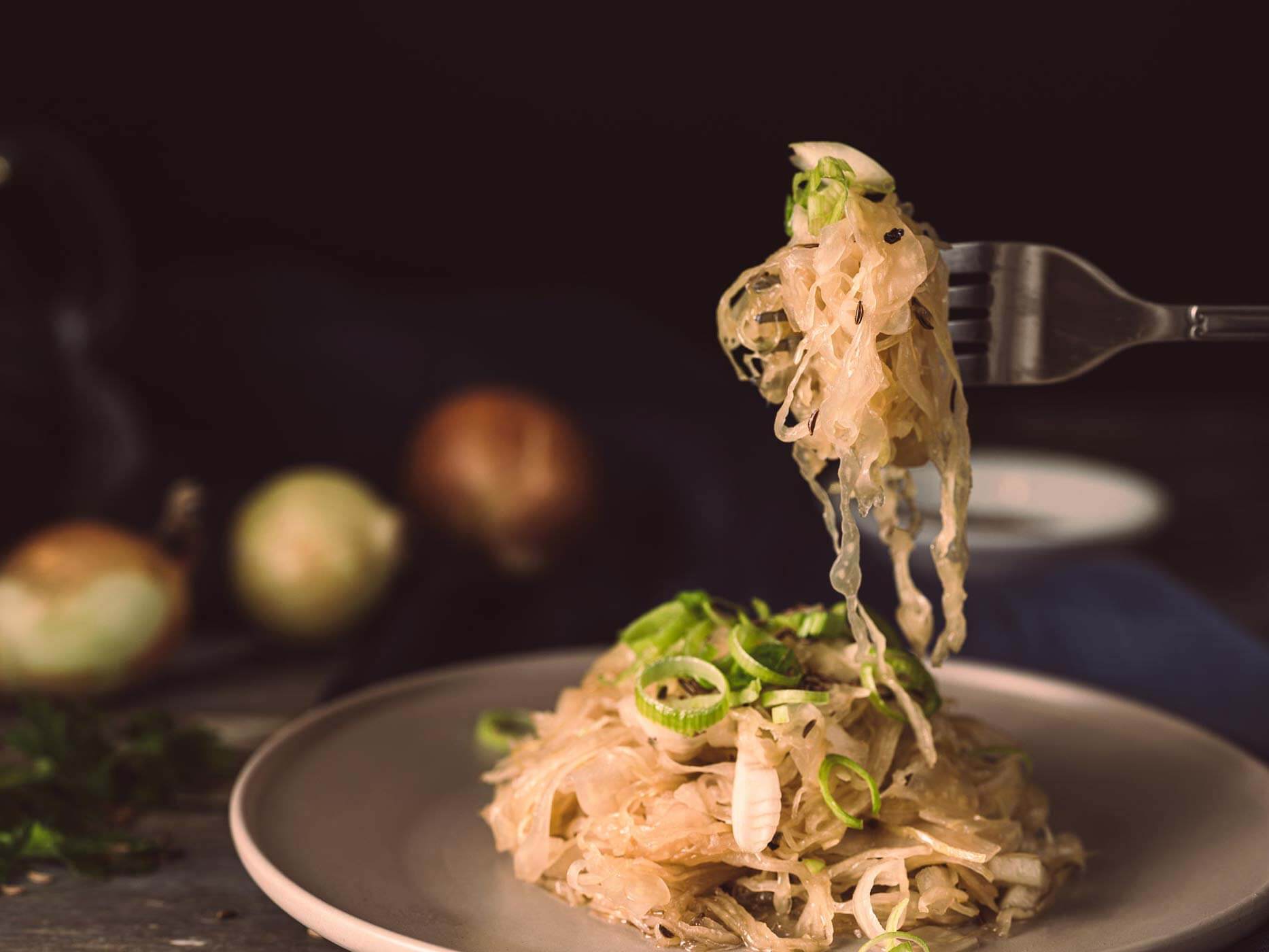 Teller mit Sauerkraut und Lauch, Gabel mit Essen darauf wird darüber gehalten