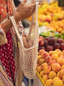 Hand hält ein Einkaufsnetz und steht vor dem Obstregal in einem Supermarkt