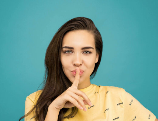 Junge Frau im gelben Shirt macht eine Pssst-Geste