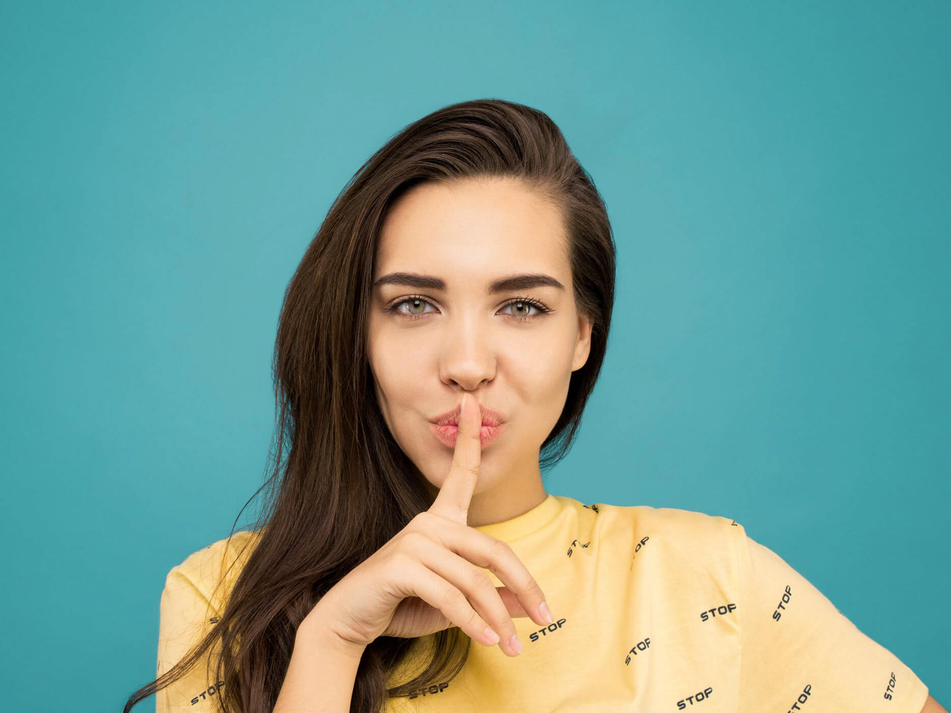 Junge Frau im gelben Shirt macht eine Pssst-Geste