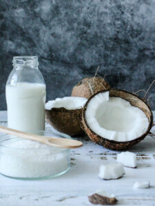 Aufgeschnittene Kokosnüsse, Kokosmilch in einer Flasche und Kokosfett in einer Schale