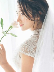 Braut im weißen Kleid mit Schleier riecht an einer weißen Rose