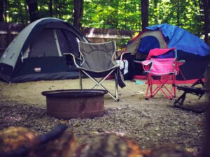 Eine Feuerschale und Campingstühle stehen vor Zelten