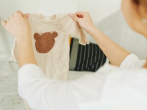 Frau hält einen Babybody mit Bärenkopf drauf in die Höhe