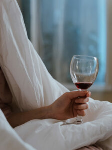 Detailbild einer Hand, die ein Rotweinglas hält, mit weißer Wäsche im Hintergrund