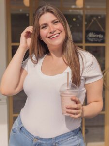 Plus Size Frau mit weißem Shirt, High Waist Jeans und Getränk in der Hand