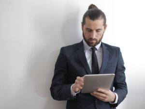 Mann mit Zopf und Tablet steht vor einer weißen Wand