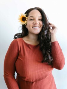 Plus Size Frau im roten, taillierten Langarmkleid und Sonnenblume im Haar