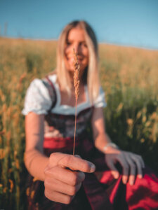 Frau im roten Dirndl hält einen Weizenhalm in die Kamera