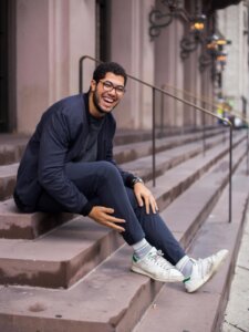 Mann mit Brille sitzt auf einer Treppe und lacht in die Kamera