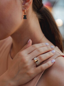 Schulter- und Halsbereich einer Frau, die ihre Hand an der Schulter hat und Gold- und Silberschmuck an Ohr und Finger trägt.