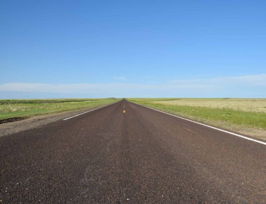 Weite Straße in den USA, die am Horizon zwischen Wiesen verschwindet