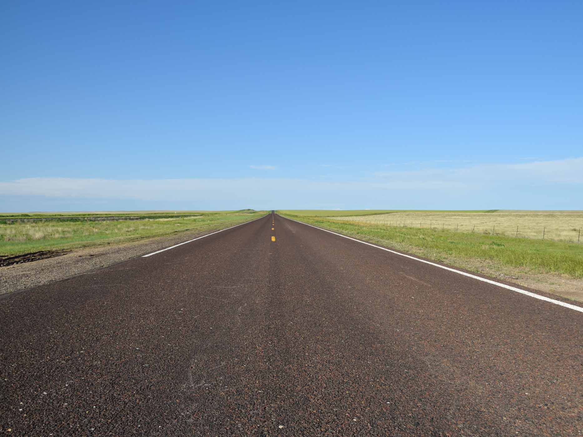 Weite Straße in den USA, die am Horizon zwischen Wiesen verschwindet