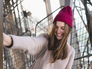 Frau mit aufgestellter roter Beanie macht draußen ein Selfie