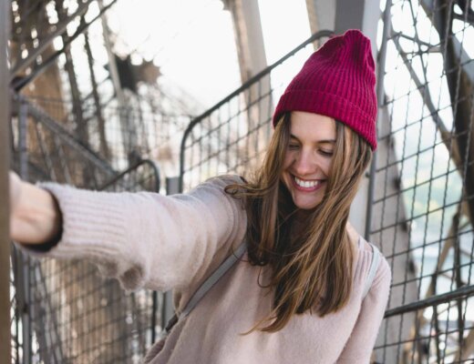 Frau mit aufgestellter roter Beanie macht draußen ein Selfie