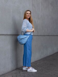Frau mit weiter Jeans steht draußen vor einer grauen Wand