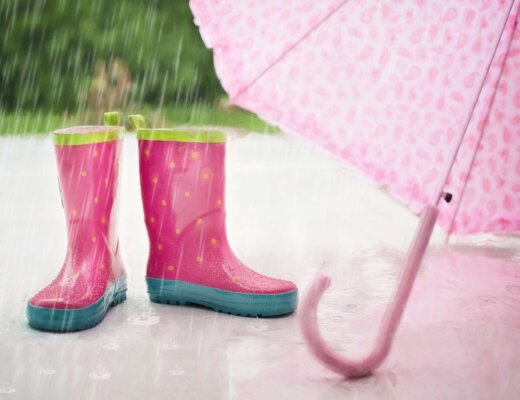 Pinke Gummistiefel und rosa Regenschirm stehen im Regen