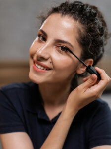 Junge Frau mit Zopf tuscht sich die Wimpern