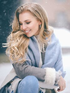 Frau sitzt draußen im Schnee und dreht sich lächelnd weg