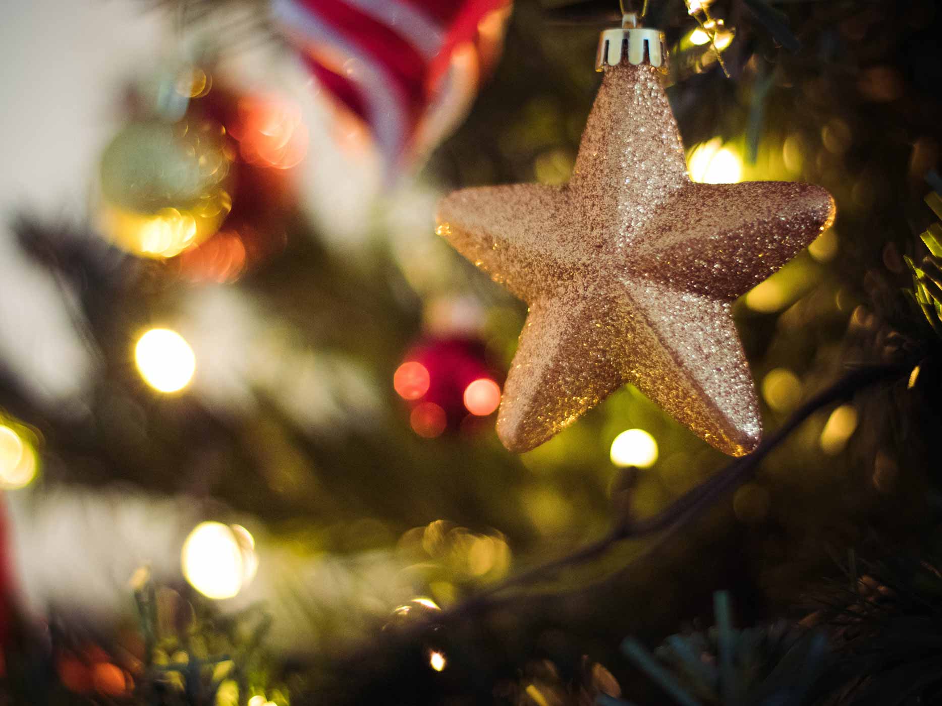 Ein goldener Stern hängt an einem festlich beleuchteten und geschmückten Weihnachtsbaum