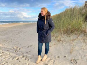 Ein Mädchen steht mit einer Winterjacke am Strand