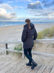 Ein Mädchen steht mit ihrer warmen Jacke am Strand