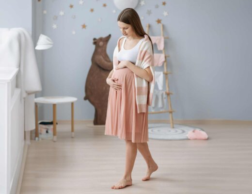 Schwangere Frau geht zufrieden lächelnd durch das Babyzimmer, während sie ihren Babybauch streichelt