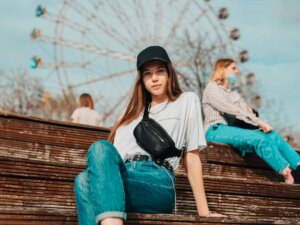 Frau sitzt auf einer Bank vor einem Riesenrad und trägt eine Bauchtasche quer über der Brust