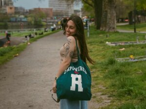 Frau steht in einem Park und trägt eine grüne Tote-Bag über der Schulter