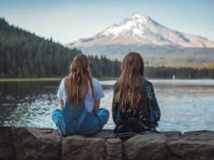 Zwei Frauen sitzen mit dem Rücken zur Kamera vor einem See.