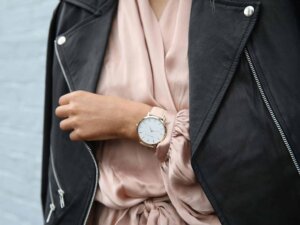 Frau trägt ein rosafarbenes Oberteil mit einer schwarzen Lederjacke und dazu eine rosafarbene Armbanduhr