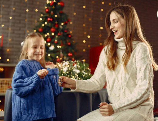 Eine Mutter hat ein weißes Strickkleid an und ihre Tochter ein blaues; sie zünden Wunderkerzen an