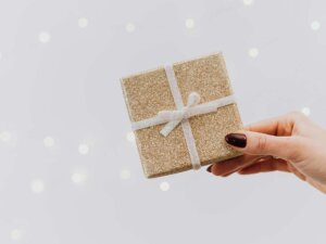 Vor einem grauen Hintergrund wird ein in goldenes Papier eingeschlagenes viereckiges Geschenk gehalten.