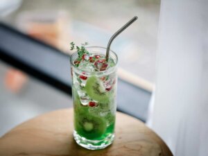Ein Glas mit einem Strohhalm und einer durchsichtigen Flüssigkeit, in der Kiwischeiben und rote Beeren schwimmen,
