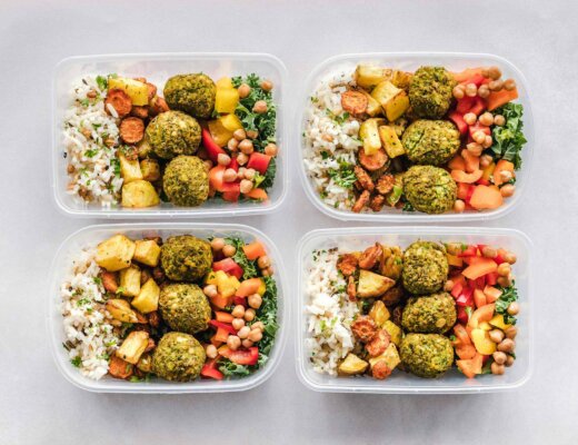 Vier Plastikbehälter sind gefüllt mir Reis, Gemüse und Falafeln.