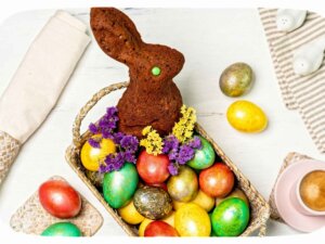 Ein brauner, gebackener Teig-Hase sitzt in einem Körbchen mit bunten Ostereiern.