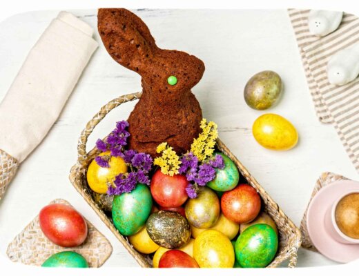 Ein brauner, gebackener Teig-Hase sitzt in einem Körbchen mit bunten Ostereiern.