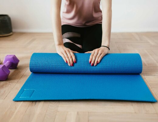 Eine Frau in Sportklamotten sitzt auf dem Boden und rollt eine blaue Sportmatte aus.