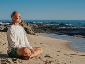 Ein Mann sitzt im Schneidersitz am Strand und genießt die Sonne.