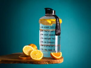 In einer Wasserflasche schwimmen mehrere Zitronenscheiben, auf der Wasserflasche sind Zeitabschnitte abgebildet, die zeigen, bis zu welcher Uhrzeit wie viel getrunken sein sollte.