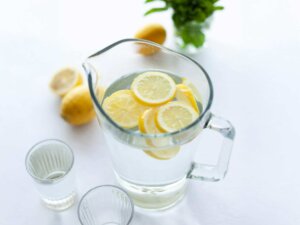 In einer Wasserkaraffe schwimmen mehrere Zitronenscheiben, daneben stehen Gläser.