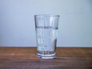 Auf einem Wasserglas steht die Aufschrift "Hey, drink water more".