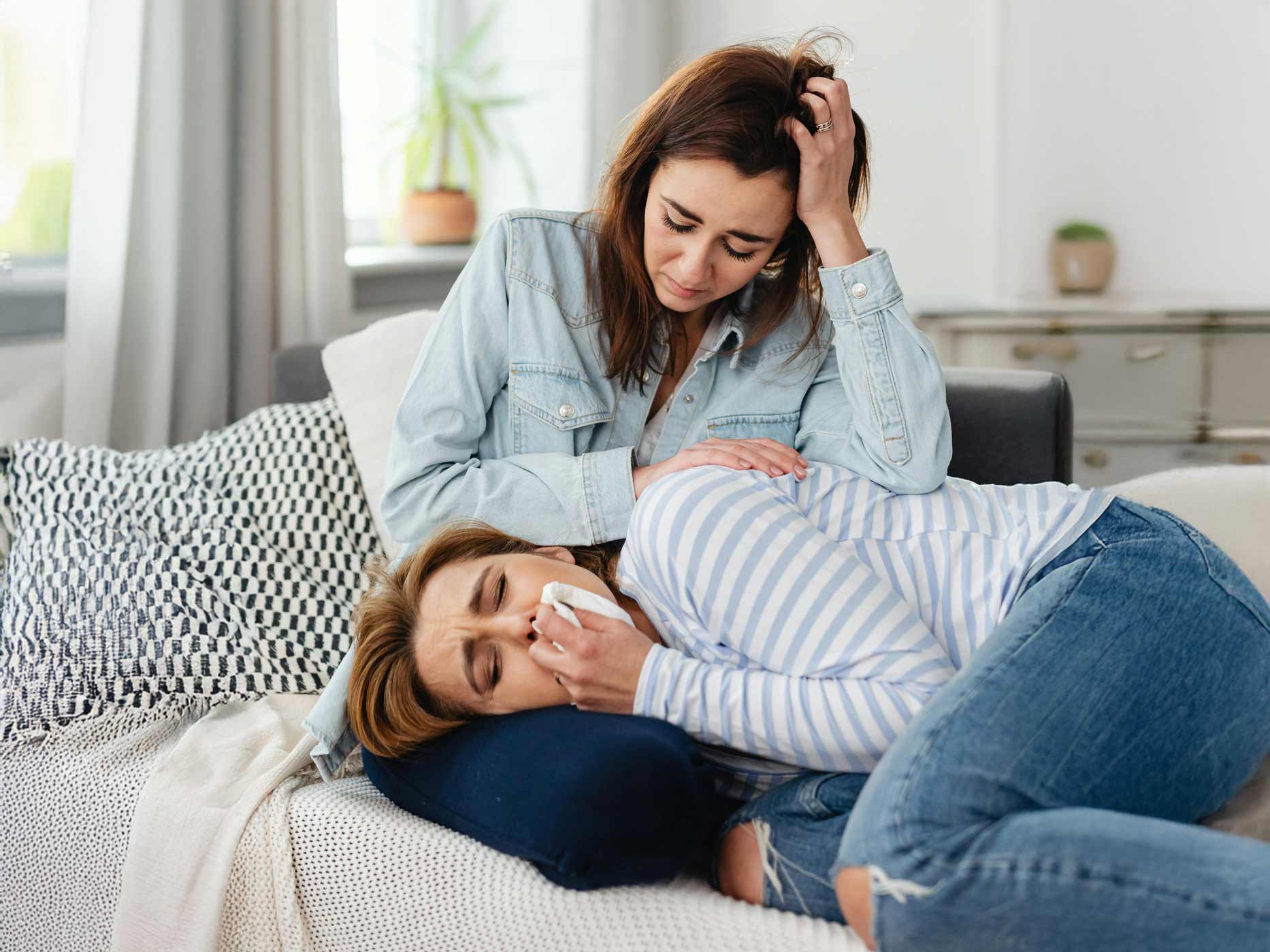 Liebeskummer loswerden Gefühle Zwei Frauen sind auf einem Sofa, die eine liegt auf dem Schoß der anderen und weint in ein Taschentuch. Die andere Frau tröstet sie.