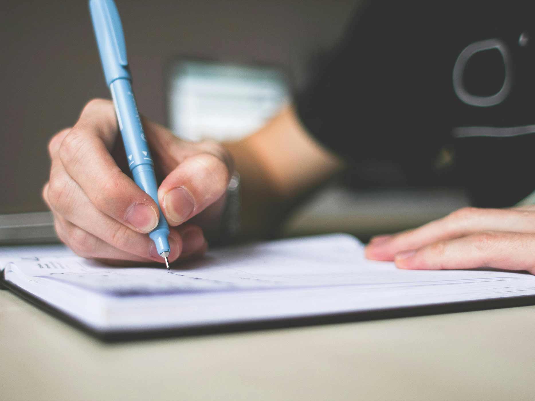 Liebeskummer loswerden Kreativität Eine Hand schreibt mit einem Stift etwas in ein Heft.